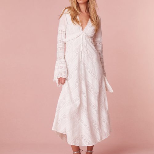 Maxi dress with long bell sleeves featuring a deep v-neck, a tiny ruffle at the waist that descends to a skirt with diagonal laces in a chevron design with textured pintuck panels. Features a zipper at the side seam.