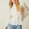 Model wearing white long sleeve blouse with button up front, lace detail, and puff shoulders.