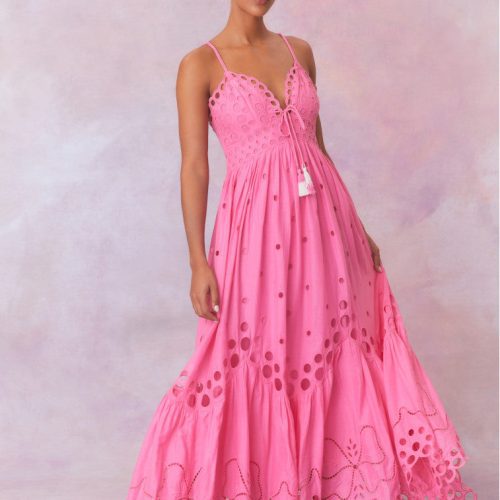 Hot pink cotton eyelet maxi dress with bow embroidery and circular eyelets all over, has spaghetti straps that criss-cross at the back, a v-neckline that descends into a sweeping skirt.