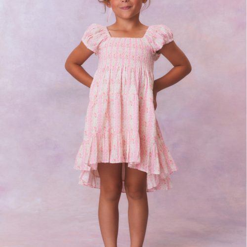 Pink floral dress for girls with flutter sleeves, a smocked top and ruffled skirt with an asymmetrical hem.